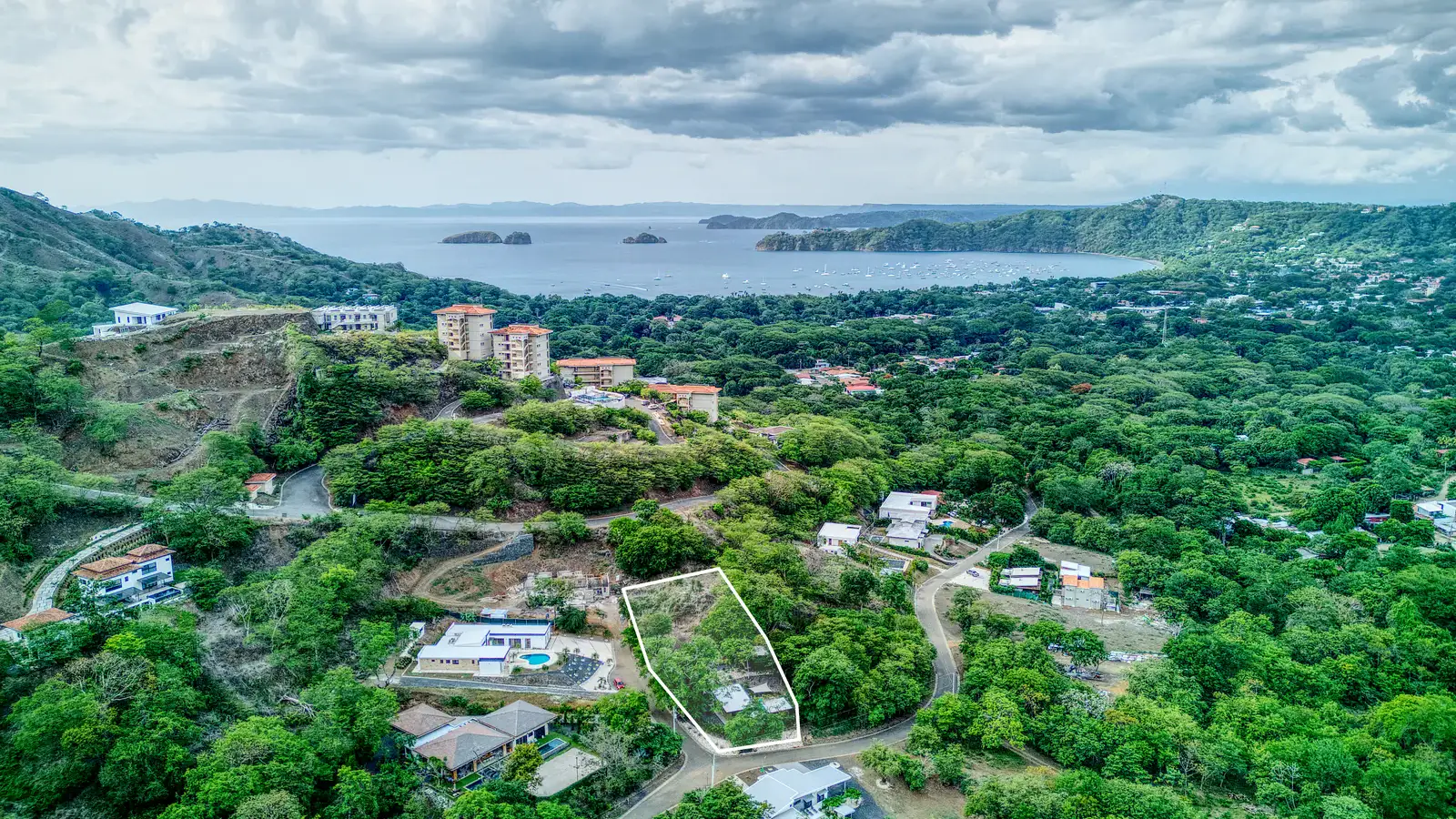 Drone still of a hillside lot outlined on screen, with the bay and town of Playas del Coco behind it